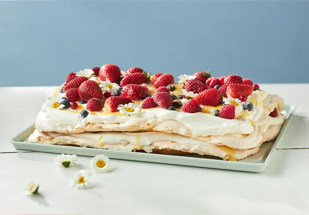 Rechteckige Baiser-Schnitten mit Lemon Curd, Sahne und frischen Erdbeeren sind mit Blüten dekoriert.