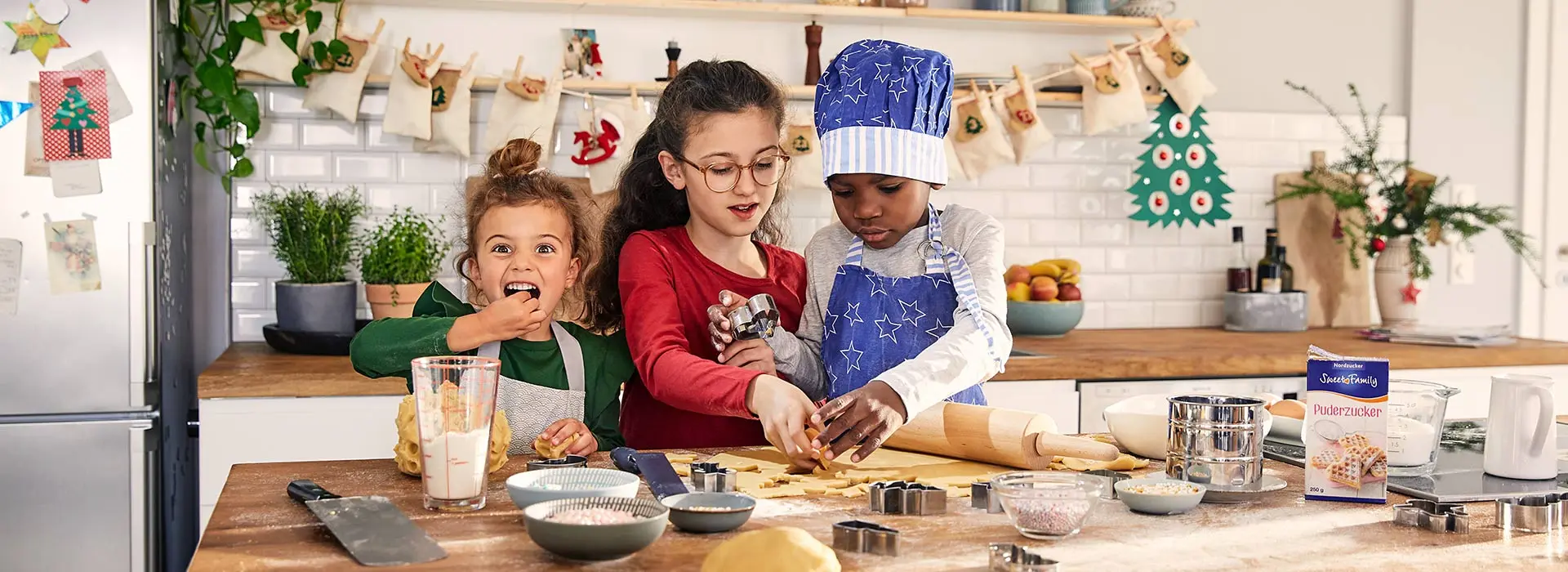 Drei Kinder stechen Plätzchen aus. Ein Mädchen guckt frech in die Kamera