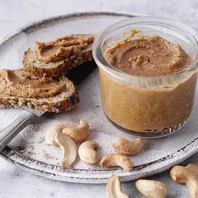 Ein Glas mit Chashewcreme steht auf einem Teller, daneben ein Brot, das mit der Creme bestrichen wurde