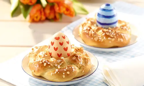 Rezept für Hefekranz mit buntem Osterei Hefezöpfe liegen auf Tellern mit bemalten Ostereiern oben drauf.