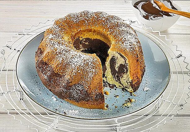 Auf einem blauen Teller liegt ein schöner runder Marmorkuchen, von dem bereits ein Stück fehlt