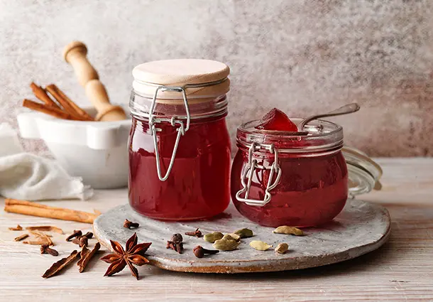 Zwei Gläser rotes Weihnachtsgelee stehen auf einem Brett mit Zimtstangen, Sternanis und Nelken