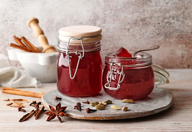 Zwei Gläser rotes Weihnachtsgelee stehen auf einem Brett mit Zimtstangen, Sternanis und Nelken