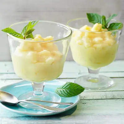 Zwei Dessertgläser mit einer gelben Dessertcreme und frischen Minzblättern 