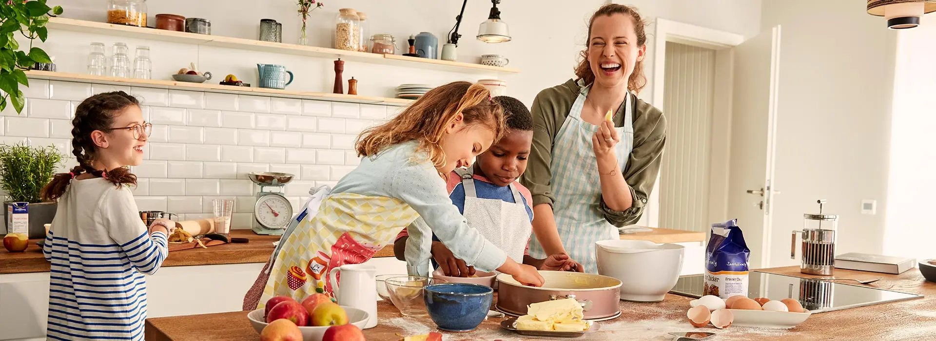 Drei Kinder und eine Frau backen zusammen und lachen ausgelassen