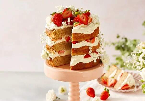 Eine mehrschichtige Erdbeertorte mit Sahne und frischen Erdbeerstücken steht auf einer Tortenplatte.