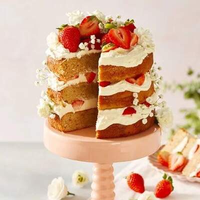Eine mehrschichtige Erdbeertorte mit Sahne und frischen Erdbeerstücken steht auf einer Tortenplatte.