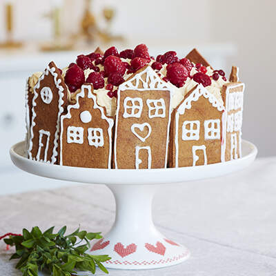 Auf einer Tortenplatte steht ein runder Kuchen, dessen Rand mit kleinen Lebkuchenhäusern verziert ist.