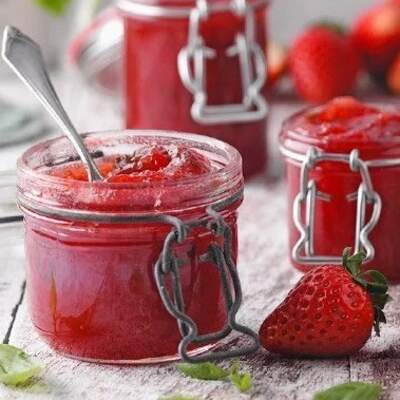 Ein Glas selbstgemachte Erdbeermarmelade mit frischen Erdbeeren und Minzblättern daneben