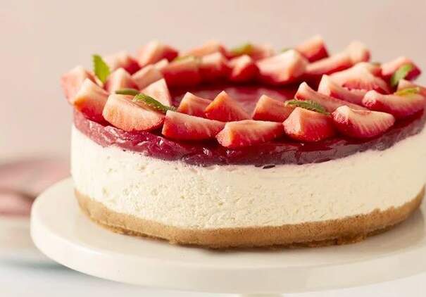 Ein runder Cheesecake mit heller Füllung ist mit Erdbeerstücken und Minzblättern belegt.