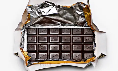 Schritt 1 Eine große Tafel dunkle Schokolade liegt in ihrer Verpackung, die oben weit geöffnet ist.