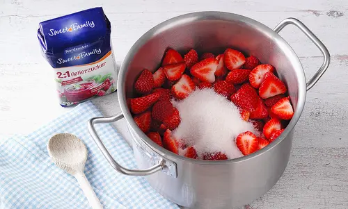 4. Die Früchte Ein Topf gefüllt mit Erdbeeren und Gelierzucker von Sweetfamily. Die verschlossene Packung steht daneben.