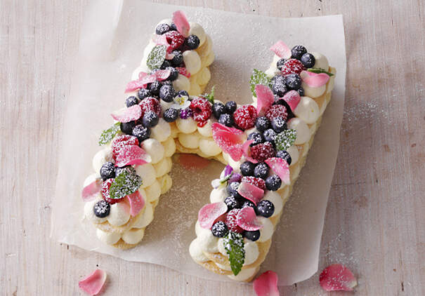 Ein großer Buchstabe aus Biskuit ist mit Buttercreme und Beeren dekoriert.