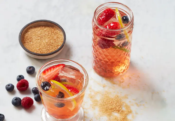 Großes Glas mit rosafarbener Sangria, gefüllt mit Erdbeerstücken, Zitrusscheiben und Eiswürfeln.