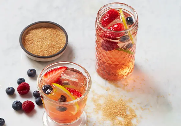 Großes Glas mit rosafarbener Sangria, gefüllt mit Erdbeerstücken, Zitrusscheiben und Eiswürfeln.