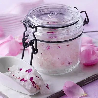 Einmachglas mit einem Zuckerpeeling aus Rosen und frischen Rosenblättern als Dekoration