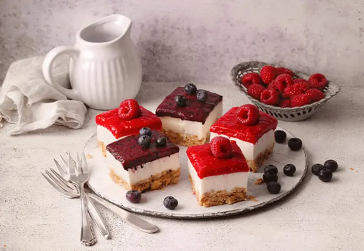 Quadratische Schnitten mit heller Quarkcreme, bedeckt von roten und violett glänzenden Fruchtspiegeln und frischen Beerenstücken.