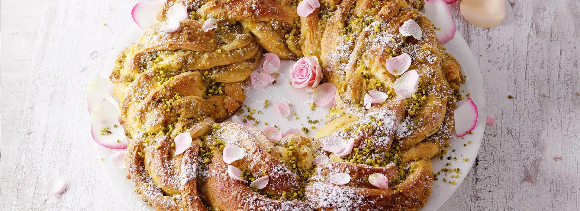 Großer Rosenzopf mit Blüten, Puderzucker und Pistazien verziert