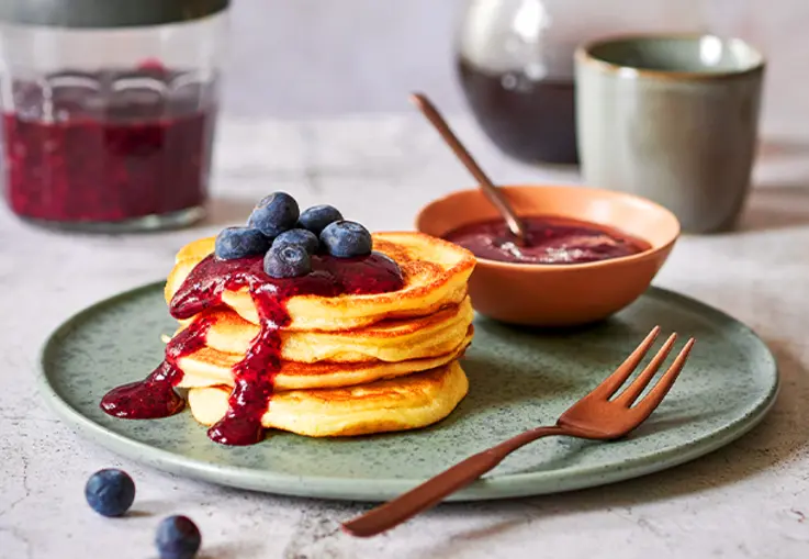 Stapel fluffiger Pancakes mit dunkler Blaubeersauce und frischen Beeren.