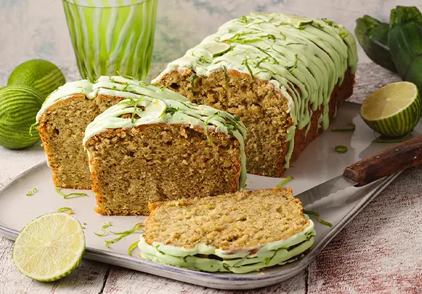 Ein goldbrauner Kasten­kuchen mit geraspelten Zucchini und gemahlenen Mandeln, der mit einem hellgrünen Limettenguss überzogen und mit feinen Limettenzesten bestreut ist