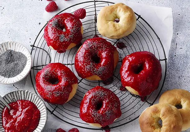 Goldene Ofendonuts mit dickem Himbeerüberzug und feinen Mohnsamen als Topping.