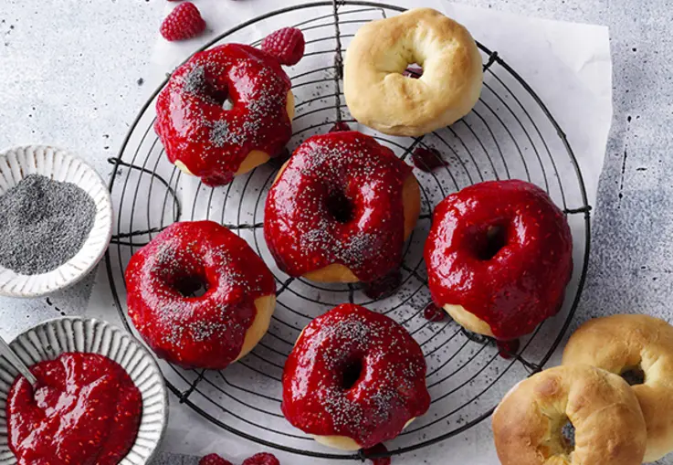Goldene Ofendonuts mit dickem Himbeerüberzug und feinen Mohnsamen als Topping.