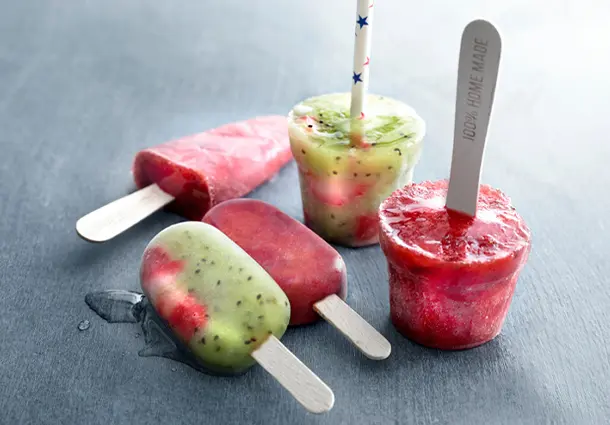 Bunte Popsicles mit roten Erdbeer‑Eisstangen und grün‑roten Eisvarianten mit Kiwistückchen, angerichtet auf Eiswürfeln