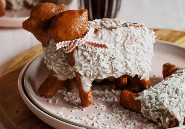 Kleine lammförmige Gebäckstücke sind mit weißem Zuckerguss und Kokosraspeln überzogen und mit Schleifen verziert