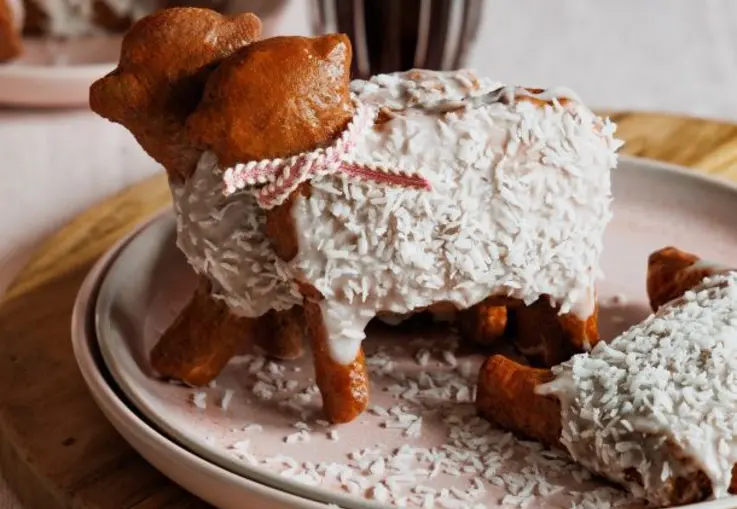 Kleine lammförmige Gebäckstücke sind mit weißem Zuckerguss und Kokosraspeln überzogen und mit Schleifen verziert