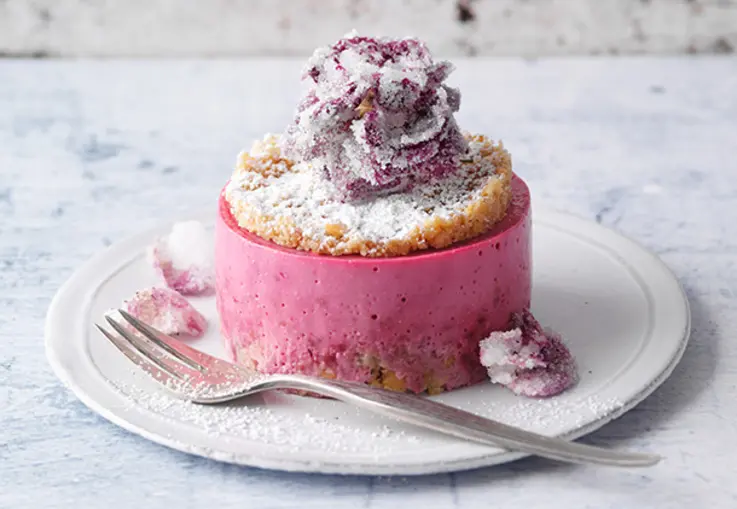 Kleine Törtchen mit rosa Creme in Rosenform, dekoriert mit frischen Himbeeren.