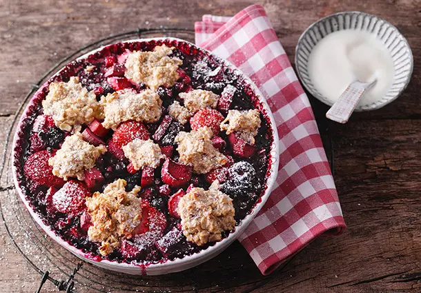 Ein Auflauf aus Haferflocken mit Rhabarberstücken und Beeren in einer Ofenform.