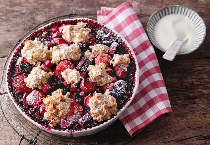 Ein Auflauf aus Haferflocken mit Rhabarberstücken und Beeren in einer Ofenform.