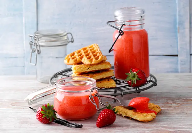 Ein Glas mit seidig rosafarbenem Erdbeer‑Vanille‑Curd, glatt gerührt und cremig, wartet mit Löffel bereit