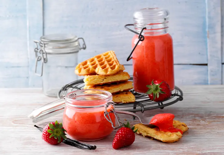 Ein Glas mit seidig rosafarbenem Erdbeer‑Vanille‑Curd, glatt gerührt und cremig, wartet mit Löffel bereit