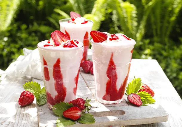 Rosa Shake mit Erdbeersirup-Spuren im Glas, getoppt mit Sahne und fruchtiger Sauce.