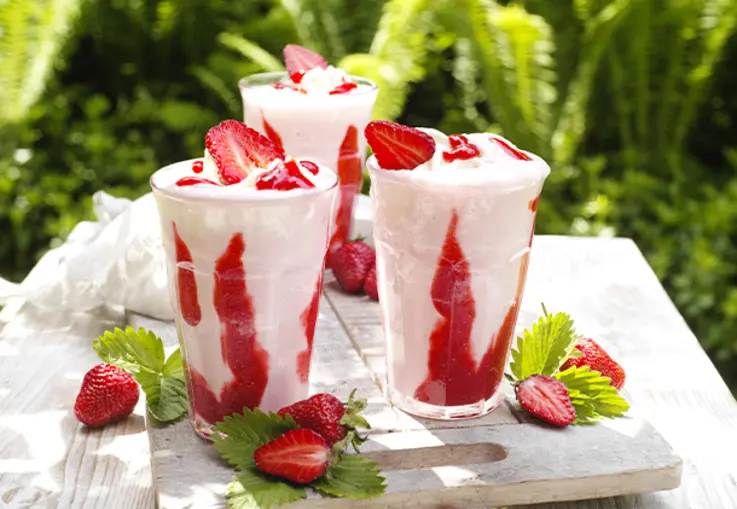 Rosa Shake mit Erdbeersirup-Spuren im Glas, getoppt mit Sahne und fruchtiger Sauce.