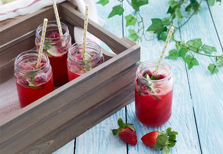 Roter Cocktail mit Limette und Minze im Glas, garniert mit Erdbeeren und Eis.