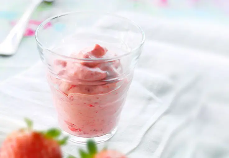 Luftiges Erdbeermousse in einem Glas wird mit frischen Erdbeeren dekoriert serviert.