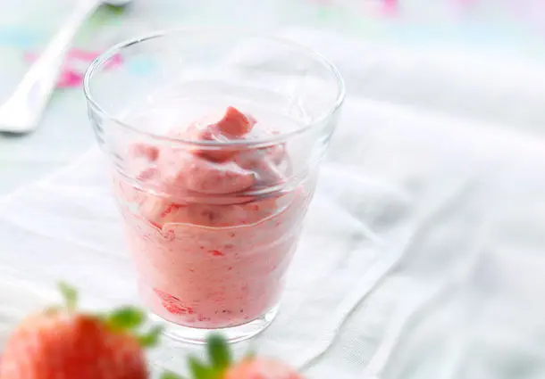 Luftiges Erdbeermousse in einem Glas wird mit frischen Erdbeeren dekoriert serviert.