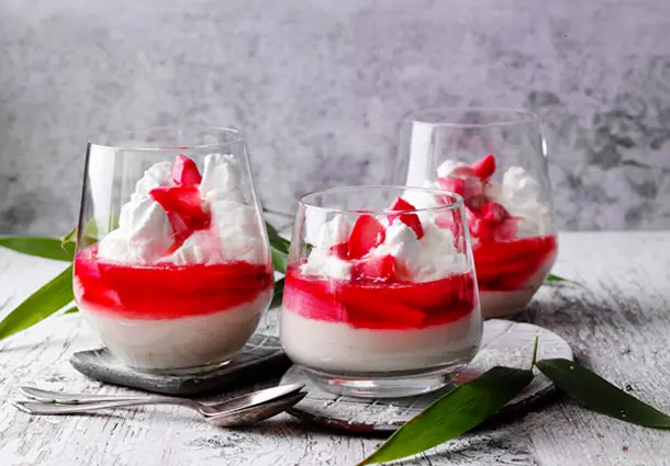 Gläser mit Kokospudding und Rhabarberkompott, oben mit Baisertupfen und Kokosraspeln verziert.