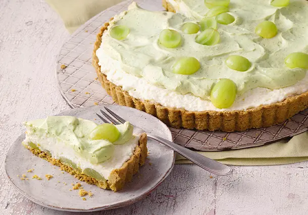 Mürbeteigtarte mit zweifarbiger Sahne-Mascarpone-Creme – weiß und hellgrün – belegt mit halben grünen Weintrauben und in Stücke geschnitten