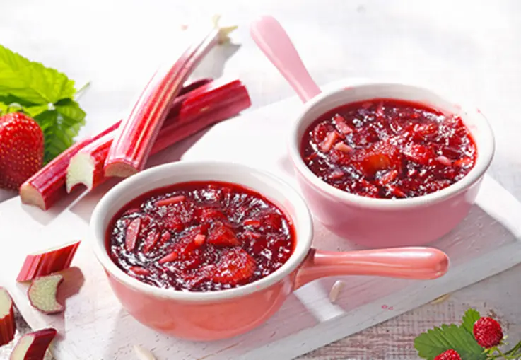 Zwei Schalen roter Rhabarber‑Erdbeer‑Crumble-Konfitüre mit frischen Erdbeeren und Rhabarber.
