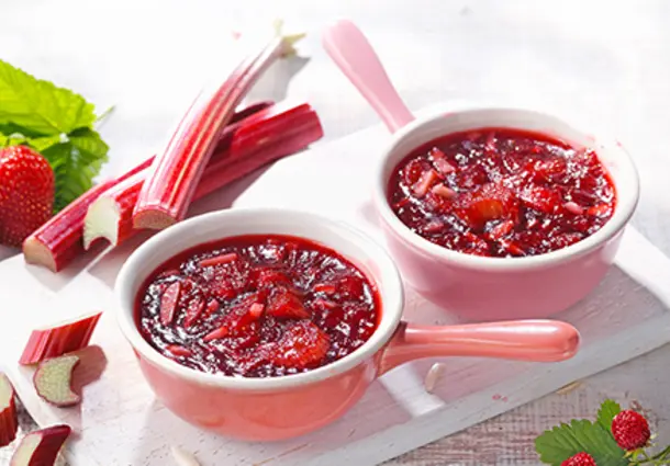 Zwei Schalen roter Rhabarber‑Erdbeer‑Crumble-Konfitüre mit frischen Erdbeeren und Rhabarber.