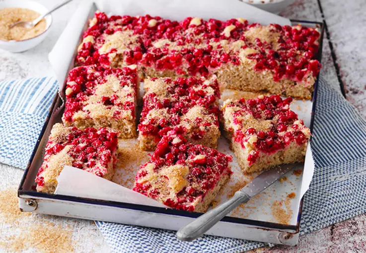 Saftiger Blechkuchen mit goldbraunen Oberfläche aus Streuseln, durchzogen von roten Johannisbeeren 
