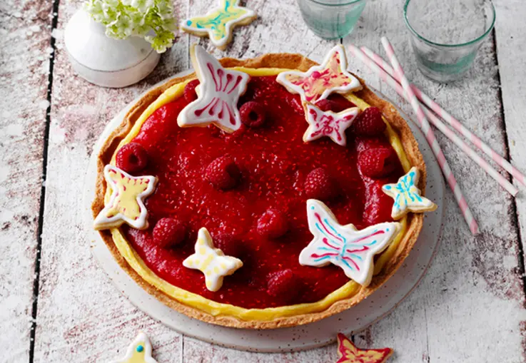Tarte mit rotem Himbeerspiegel, dekoriert mit Schmetterlingskeksen und frischen Beeren.