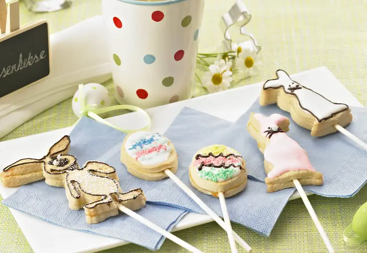 Lollies aus Mürbeteig in Form von Hasen, Küken und Eiern, auf Stielen gesteckt und mit Zuckerguss sowie bunten Streuseln dekoriert