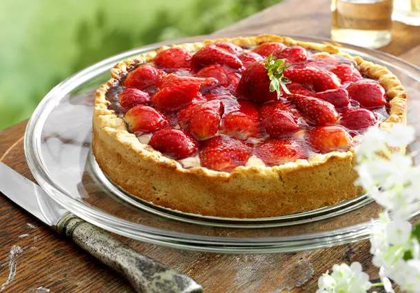 Runde Tarte mit knusprigem Mandelmürbeteig, darauf glänzende halbe Erdbeeren in dichten Reihen auf sahniger Füllung
