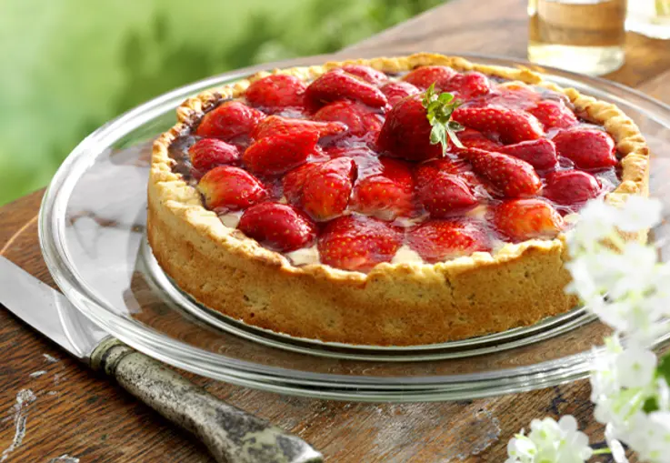 Runde Tarte mit knusprigem Mandelmürbeteig, darauf glänzende halbe Erdbeeren in dichten Reihen auf sahniger Füllung