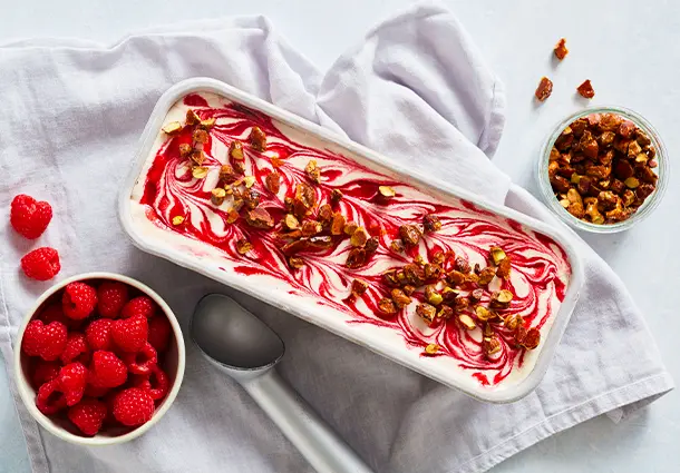 Gefrorene Scheiben aus rosa‑weißer Semifreddo‑Masse zeigen Himbeermarmorierung und sind mit karamellisierten Pistazienstückchen bestreut