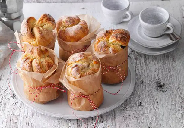 Mehrere kleine Panettoni aus Hefeteig, gefüllt mit kandierten Zitrusfrüchten und Rosinen, in Papierförmchen gebacken und mit Zucker bestreut